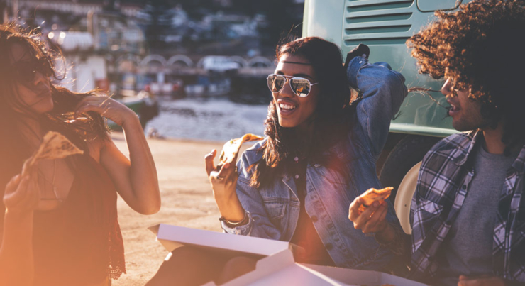 a group of young adults eating pizza outside