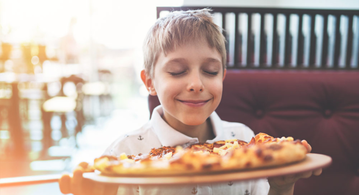 a little boy with his eyes closed smelling pizza