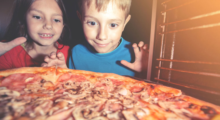 a little boy and little girl looking at a pizza in the oven