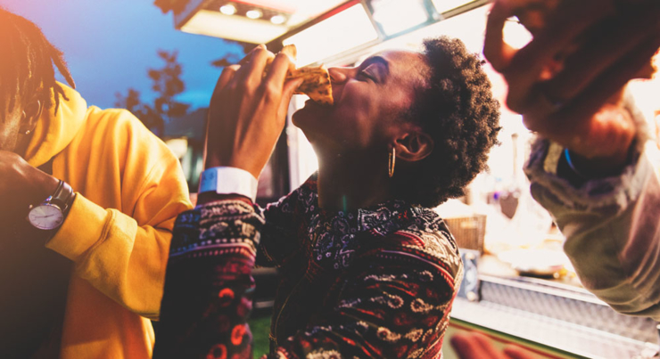 a woman eating a slice of pizza surrounded by friends