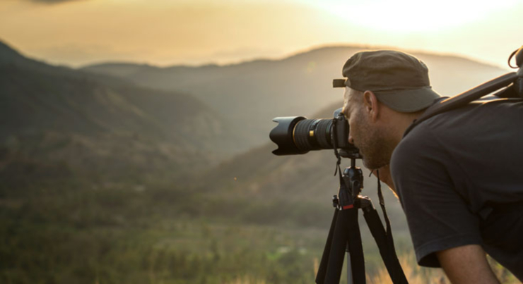 man looking through a telescope into the green mountains